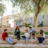 A group of five people sit and laugh together under trees.